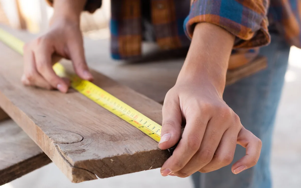 Hands marking a wood board with a tape measure and pencil
