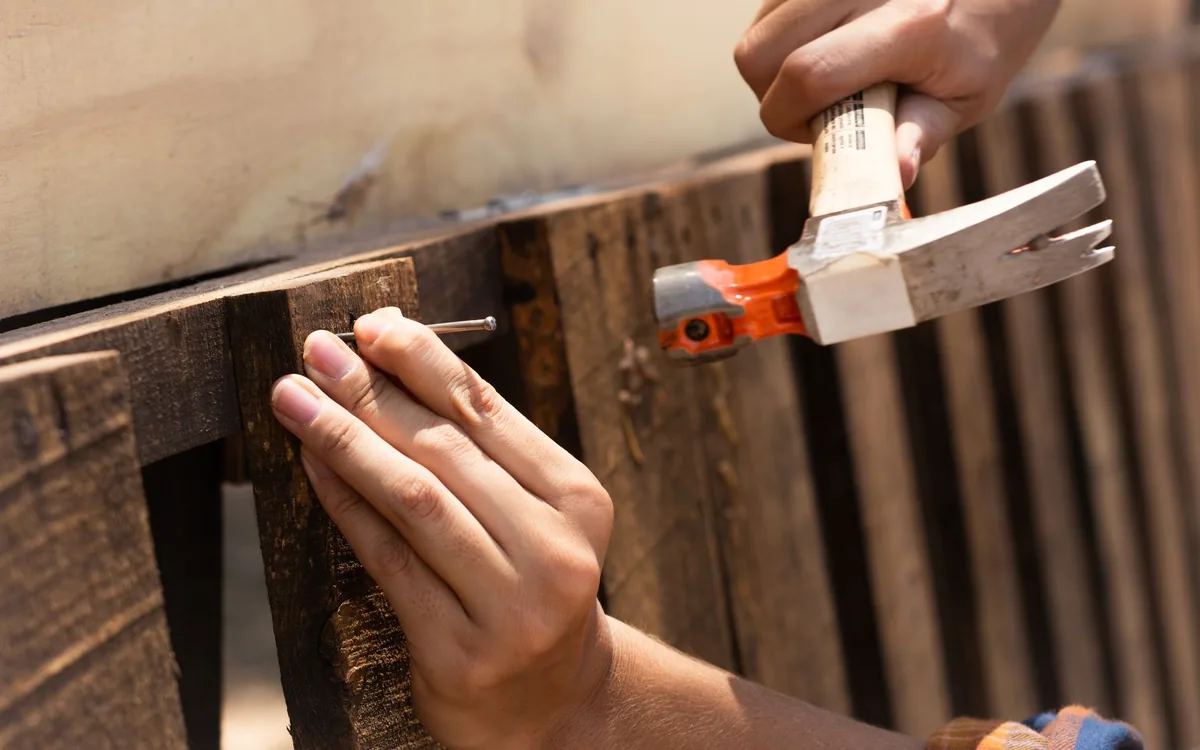 Hands hammering a new board onto a wood fence